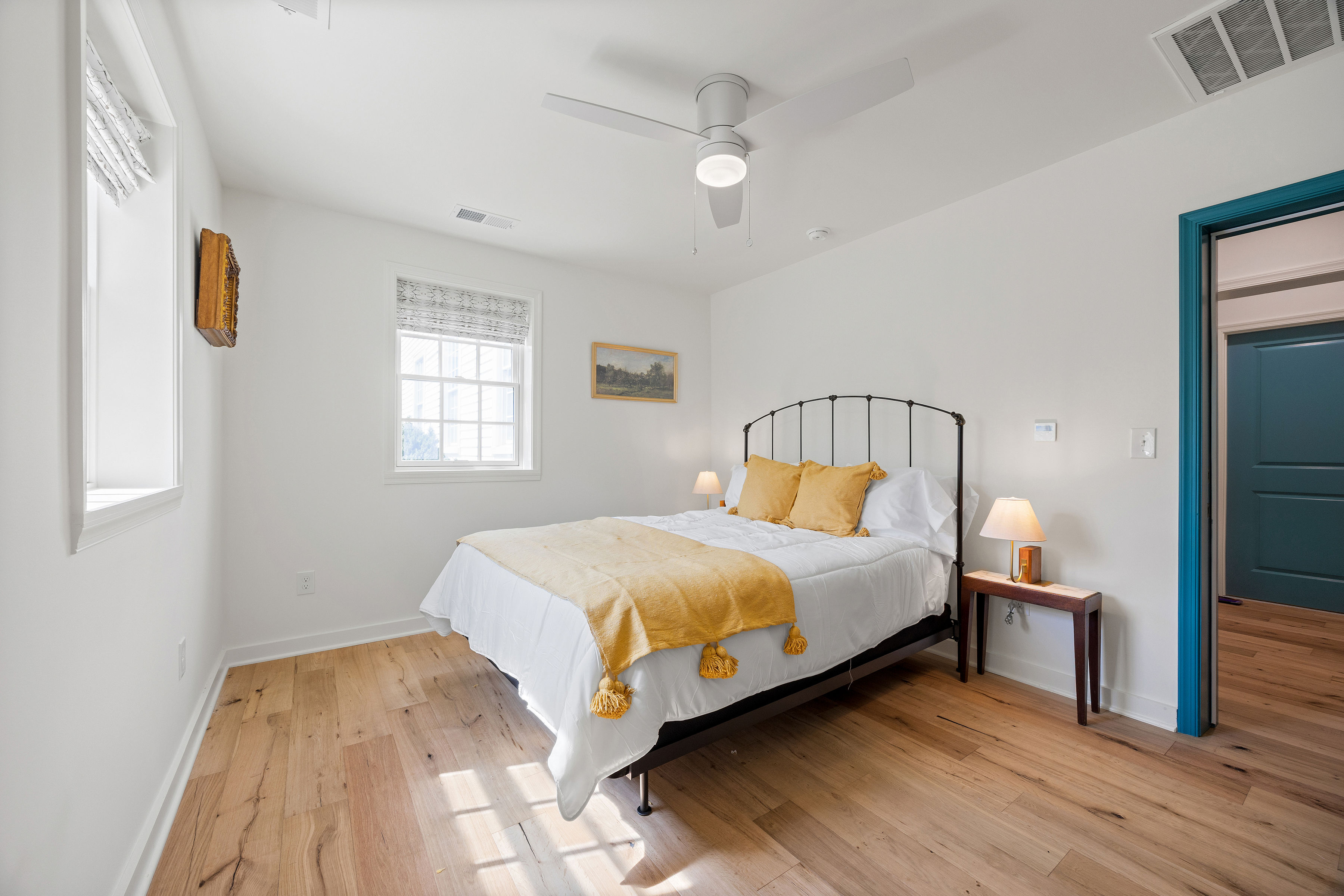 A bright, minimalist bedroom featuring a double bed with yellow accents and wooden flooring.